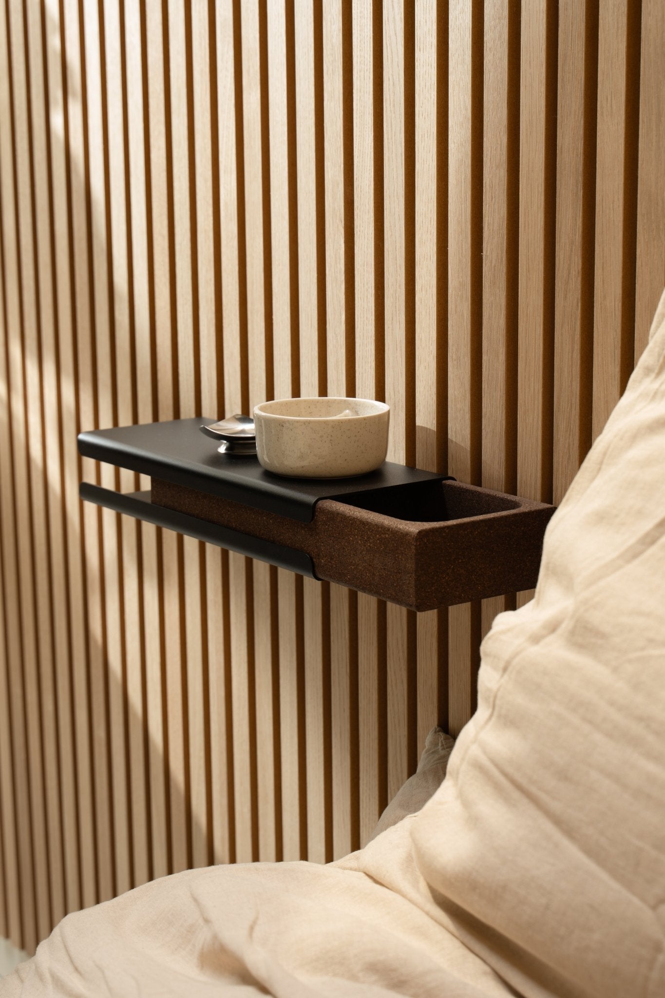 Minimalist wall shelf with a ceramic bowl and WoodUpp Norr Key Tray beside a beige cushion and Akupanel acoustic panel, illuminated by soft natural light.